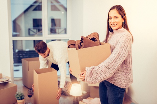 Wife wearing warm sweater holding box while moving in new house